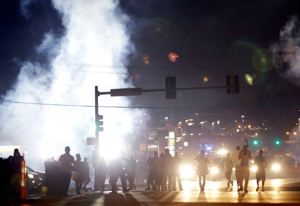 In this Monday, Aug. 18, 2014 file photo, people stand near a cloud of tear gas in Ferguson, Mo. during protests for the Aug. 9 shooting of unarmed black 18-year-old Michael Brown by a white police officer. The U.S. government agreed to a police request to shut down several miles of airspace surrounding Ferguson, even though authorities said their purpose was to keep media helicopters away during protests in August, according to recordings of air traffic control conversations obtained by The Associated Press.    (AP Photo/Jeff Roberson)