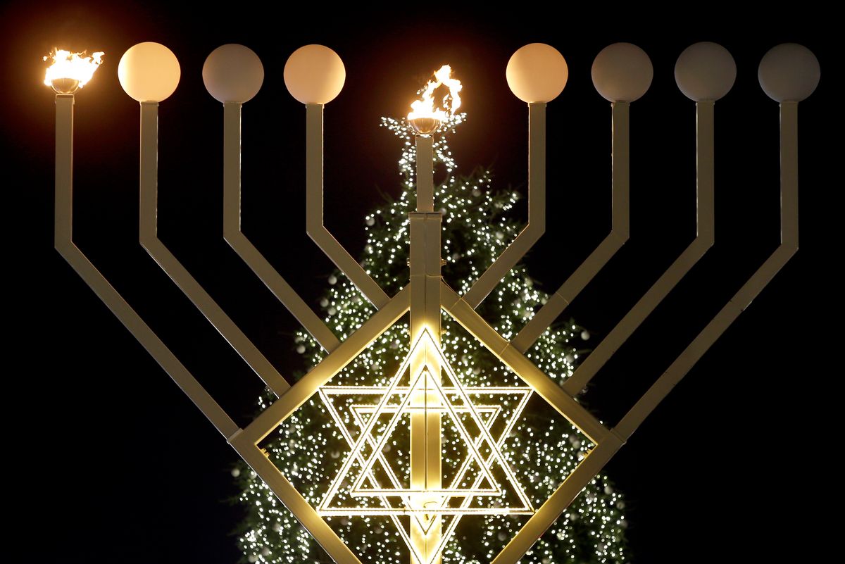 FILE - In this Tuesday, Dec. 16, 2014 file photo, the first flames of a a giant Hanukkah Menorah in front of a Christmas tree at the Brandenburg Gate in Berlin, Germany, burn at the launch of the eight-day Jewish Festival of Lights, named Hanukkah. The lights were inflamed by German Interior Minister Thomas de Maiziere and Rabbi Yehuda Teichtal. (AP Photo/Michael Sohn, File) (AP)