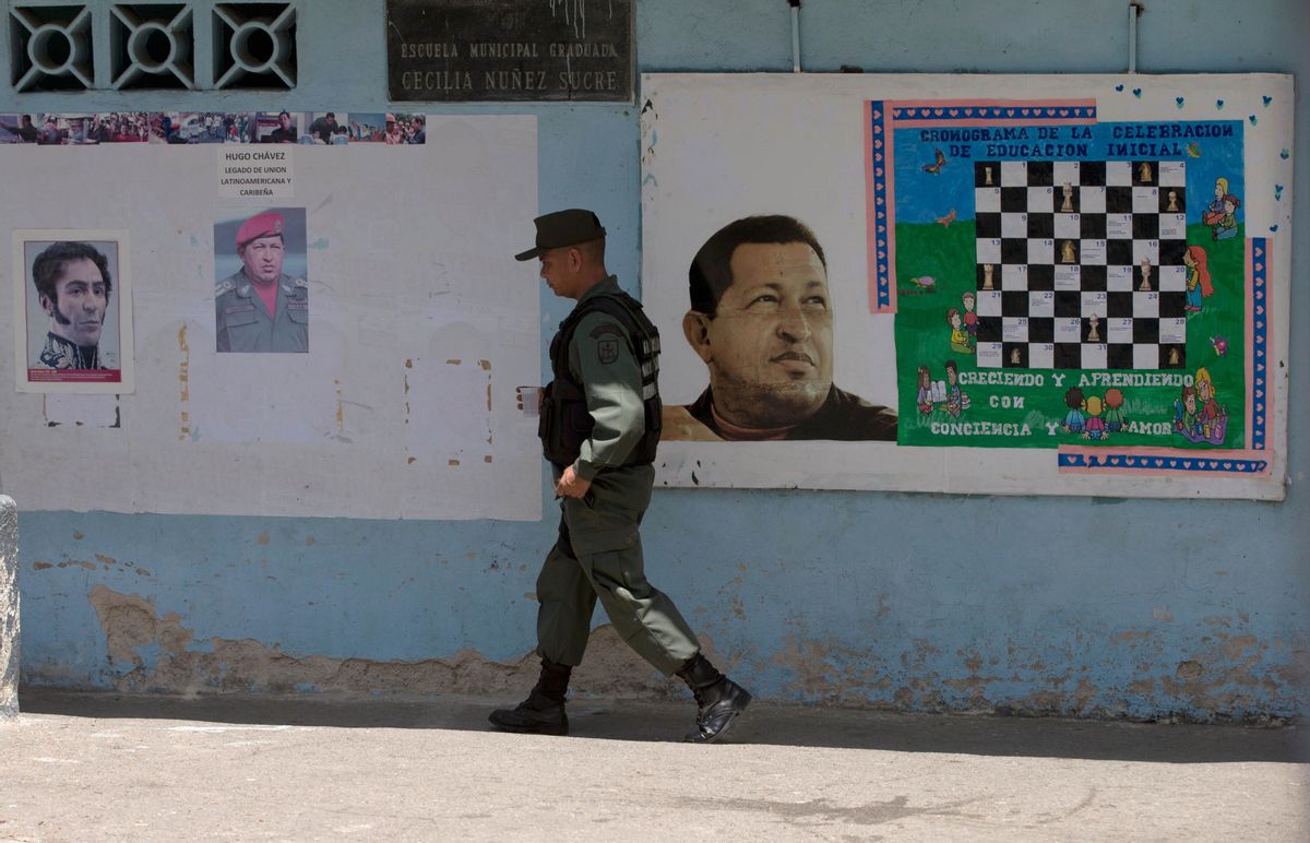 A Bolivarian National Guards officer walks near images of the late Venezuelan President Hugo Chavez and Independence hero Simon Bolivar, left, at a poll station in Caracas, Venezuela, Sunday, May 17, 2015. Venezuelans are voting to select the opposition leaders who will run against the ruling socialist partys candidates in upcoming legislative elections thought to be government critics first chance at an electoral victory in years. (AP Photo/Fernando Llano) (AP)