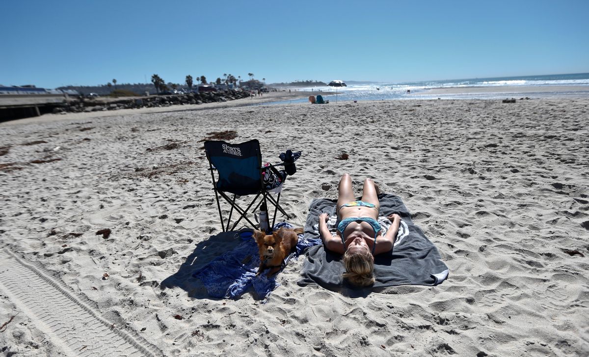 Kim McIntyre, from LaJolla, Calif., along with her dog Benji rest on the beach in Encinitas, Calif., Tuesday, Feb. 16, 2016. California is having another day of unseasonable warmth before a low-pressure system brings rain and snow. (AP Photo/Lenny Ignelzi) (AP)