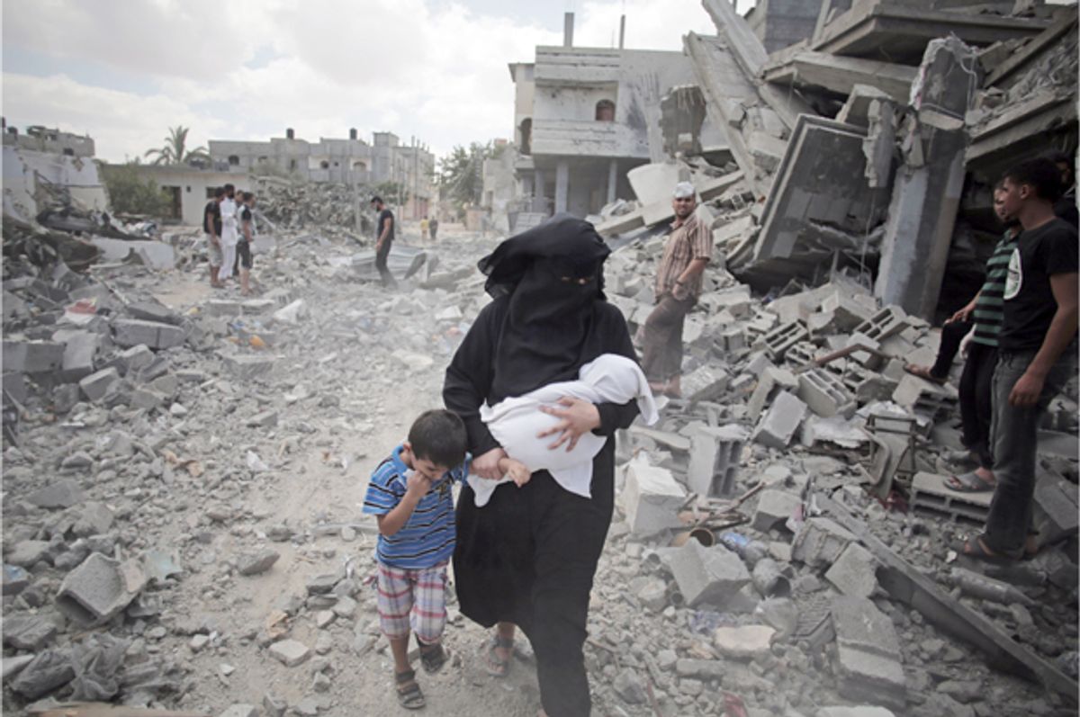 A Palestinian woman passes by rescuers inspecting the rubble of destroyed houses following Israeli strikes in Rafah refugee camp, southern Gaza Strip.  (AP/Khalil Hamra)