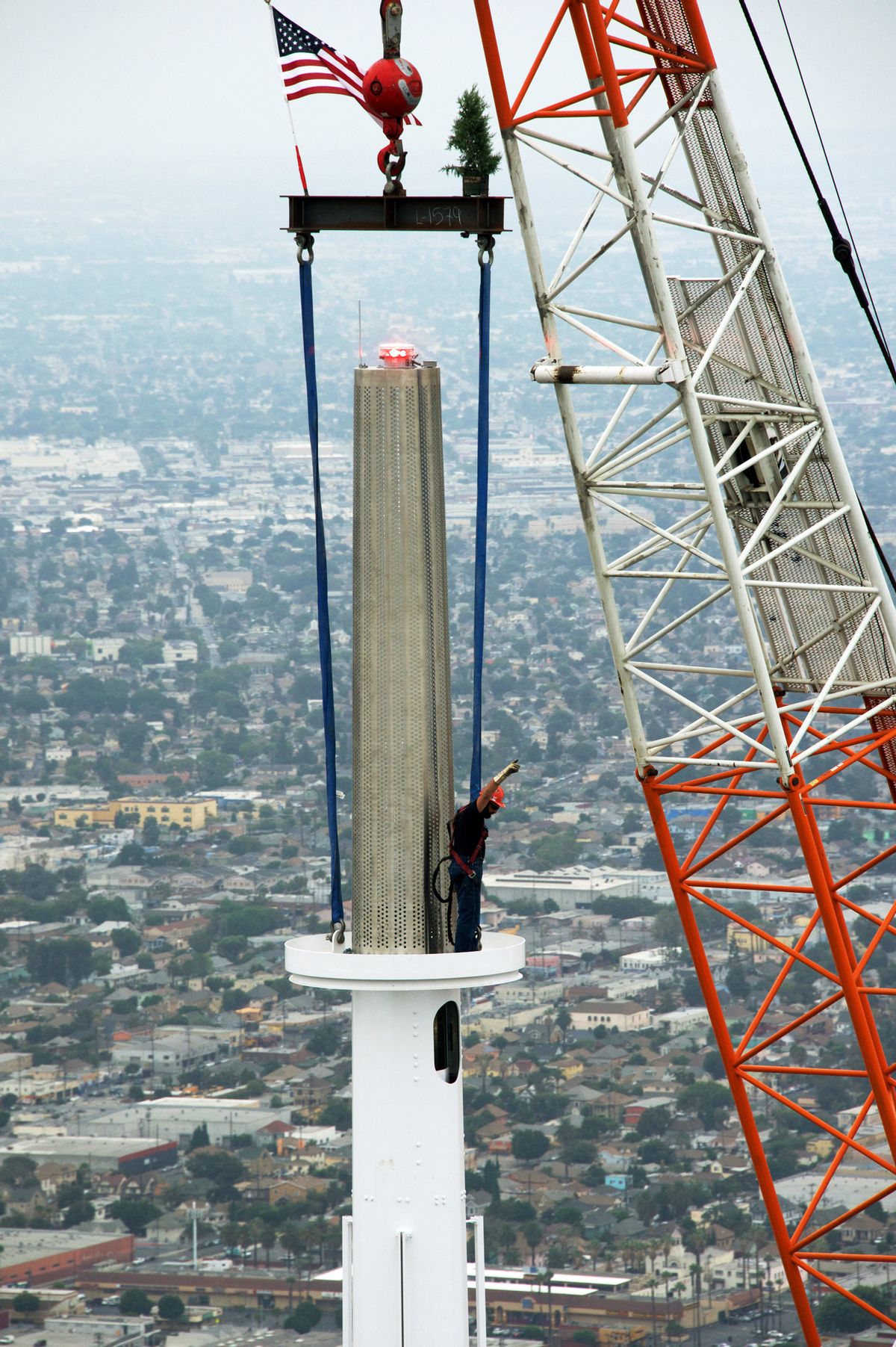 In this photo provided by the Wilshire Grand Center, a worker signals as a crane hoists a beacon into place atop a 160-foot spire on the Wilshire Grand Tower early Saturday, Sept. 3, 2016, in downtown Los Angeles. The 10-ton spire makes the structure the tallest building west of the Mississippi River. The $1 billion hotel and office complex is scheduled to open next March. (Gary Leonard/Wilshire Grand Center via AP) (AP)