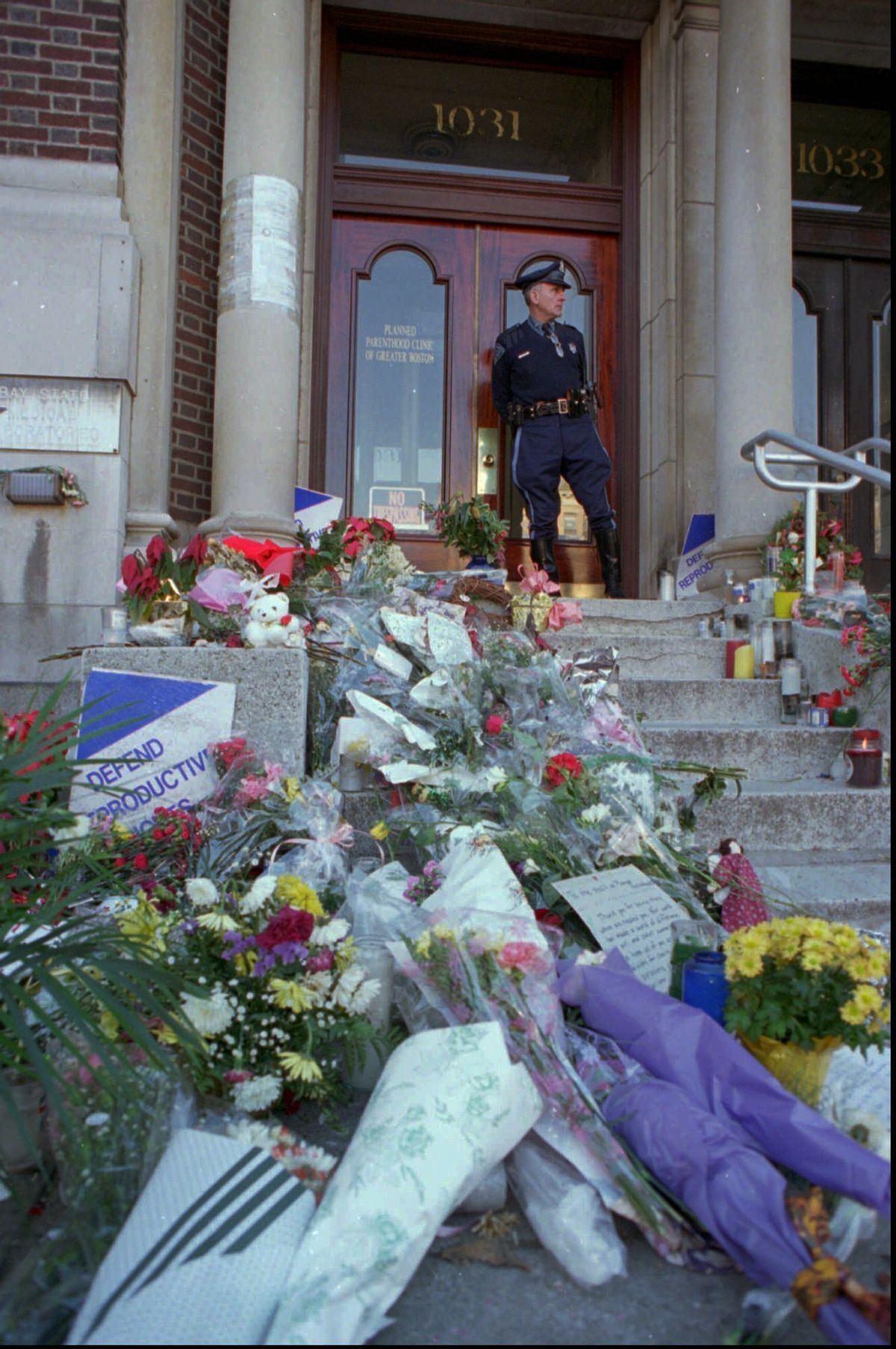 FILE - In this Wednesday, Jan. 4, 1995 file photo, Masssachusetts State Trooper Daniel Dhionis stands guard at the Planned Parenthood Clinic of Greater Boston in Brookline, Mass,, where flowers and letters were left after two women were killed, and five people injured in shootings at Planned Parenthood and another clinic. Planned Parenthood clinics have been repeated targets of bombings, arson and protests. (AP Photo/Julia Malakie) (AP)
