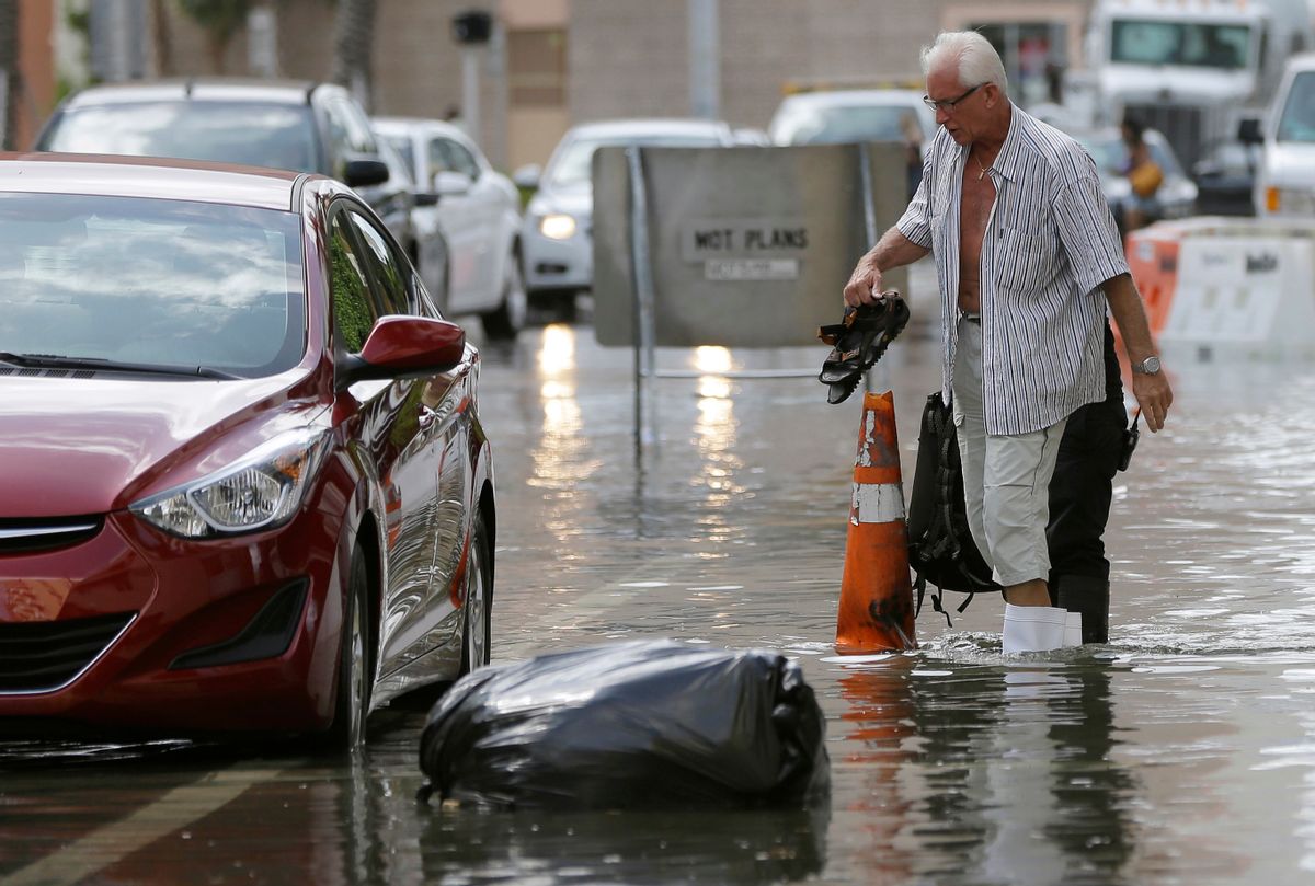 FILE - In this Sept. 30, 2015 file photo, a hotel guest carries his shoes as he is escorted to his car along in Miami Beach, Fla. The street flooding was in part caused by high tides due to the lunar cycle, according to the National Weather Service. A new scientific report finds man-made climate change played some kind of role in two dozen extreme weather events around the world in 2015. But it also detected no global warming fingerprints in a handful of other weird weather instances. (AP Photo/Lynne Sladky, File) (AP)