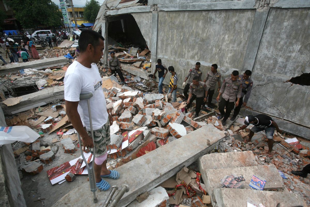 Faisal Marwan, left, who was injured in Wednesday's earthquake, stands on the ruins of his shop as police officers clear the rubble in Tringgading, Aceh province, Indonesia, Friday, Dec. 9, 2016. Over a hundred of people were killed in the quake that hit the northeast of the province on Sumatra before dawn Wednesday. Hundreds of people were injured and thousands buildings destroyed or heavily damaged. (AP Photo/Binsar Bakkara) (AP)