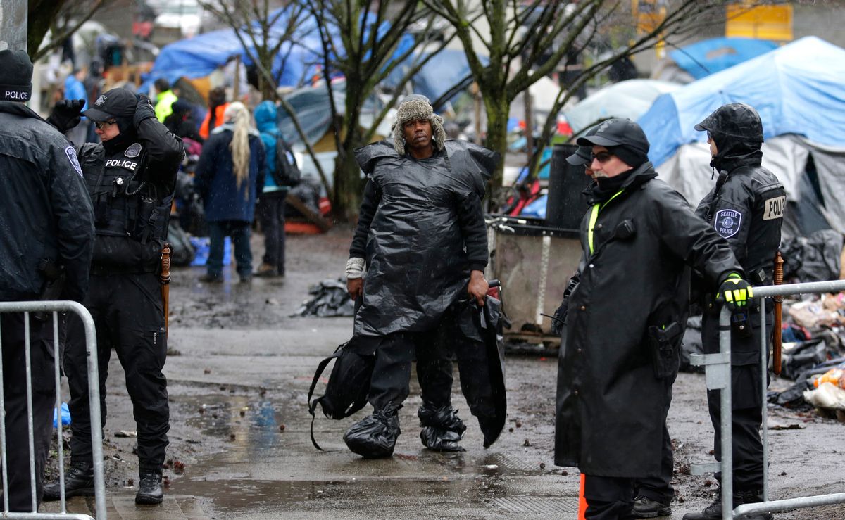 In this March 7, 2017 photo, a man wearing plastic bags in the rain carries belongings as he walks during a sweep to clear out people living at a homeless encampment known as "The Field," in Seattle's Stadium district south of downtown. Sixteen months after he declared a state of emergency on homelessness, Seattle’s mayor is asking voters in this liberal, affluent city for $55 million a year in new taxes to fight the problem. (AP Photo/Ted S. Warren) (AP)