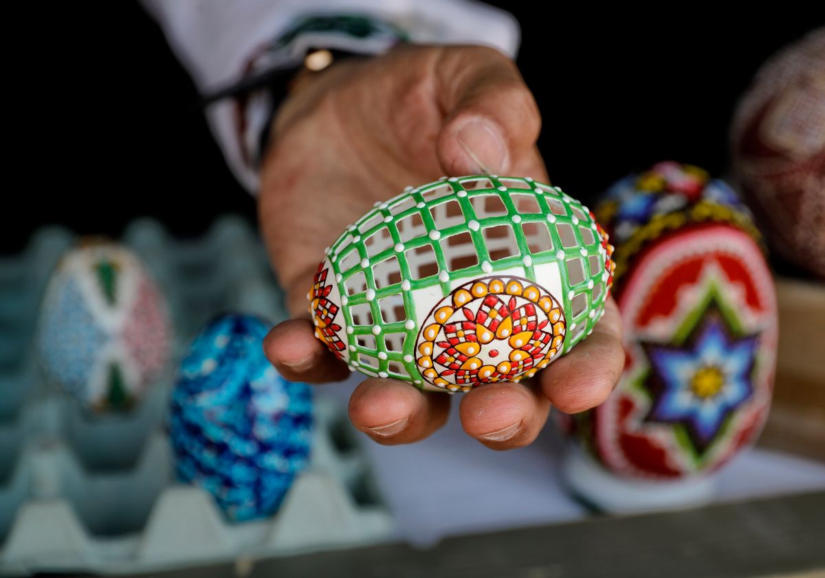 In this Thursday, April 13, 2017, picture artisan Nicu Poenariu displays for a photograph an Easter egg on sale at a fair in Bucharest, Romania. Ahead of Easter, celebrated by both Orthodox and Catholic believers on April 16 processions of priests clad in golden robes carrying foliage on Palm Sunday in a recreation of Jesus' ride into Jerusalem, mixed with more commercial flavored celebrations like an Easter fair outside the giant palace built by late Communist leader Nicolae Ceausescu where entertainers strutted around wearing giant rabbit heads.(AP Photo/Vadim Ghirda) (AP)
