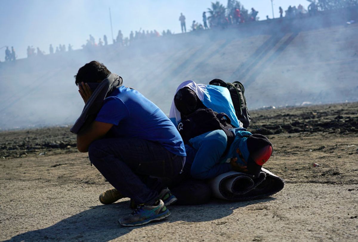 Three Honduran migrants huddle in the riverbank amid tear gas fired by U.S. agents on the Mexico-U.S. border after they and a group of migrants got past Mexican police at the Chaparral border crossing in Tijuana, Mexico, Sunday, Nov. 25, 2018 (AP/Ramon Espinosa)