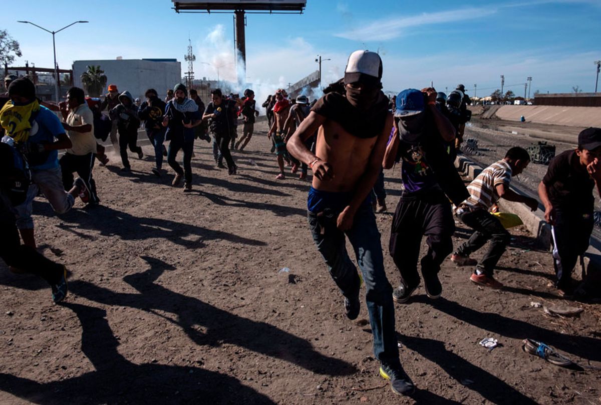 Central American migrants -mostly Hondurans- run along the Tijuana River near the El Chaparral border crossing in Tijuana, Baja California State, Mexico, near US-Mexico border, after the US border patrol threw tear gas from the distance. (Getty/Guillermo Arias)