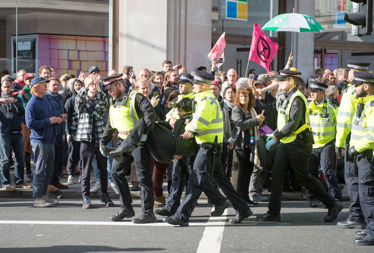 Police arrest an activist as hundreds of members of the Extinction Rebellion environmental activist group swarm Oxford circus with three activists erecting a road blocking wooden pyramid structure with an upside down tree hanging in the middle on October 18, 2019 in London, England. (Photo by Ollie Millington/Getty Images)
