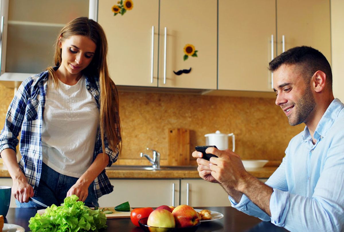 Man playing video game on smartphone while his girlfriend cooking (Getty Images)