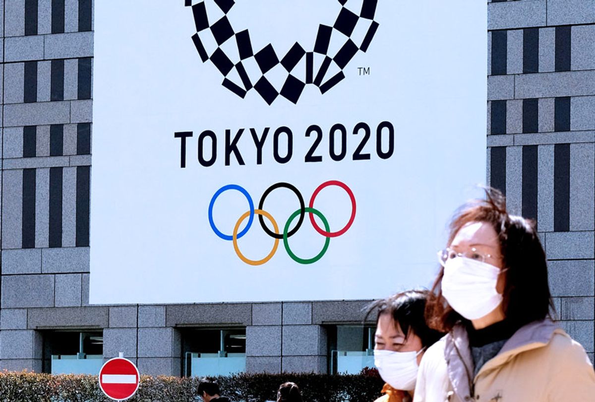 Pedestrians wearing face mask walk before the logo of the Tokyo 2020 Olympic Games displayed on the Tokyo Metropolitan Government building in Tokyo on March 24, 2020. (KAZUHIRO NOGI/AFP via Getty Images)