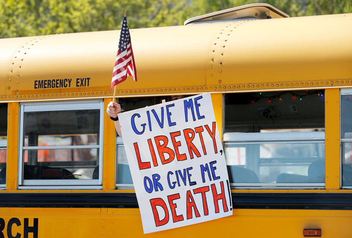 A person holds a sign while waving a flag in the direction of people gathered to voice their opposition to stay-at-home orders put into place due to the COVID-19 outbreak outside the Missouri Capitol (AP Photo/Jeff Roberson)