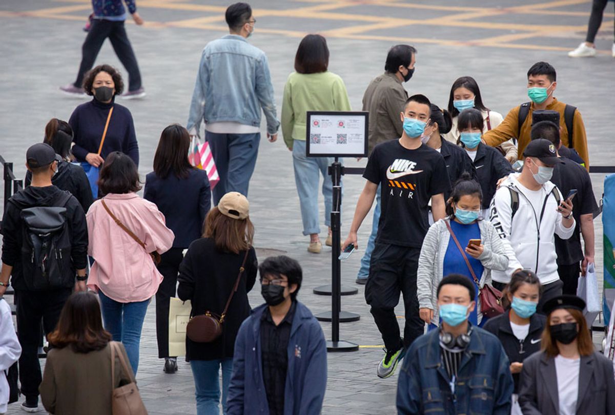 People wear face masks to protect against the spread of the new coronavirus as they walk through a temperature checkpoint at an outdoor shopping area in Beijing (AP Photo/Mark Schiefelbein)