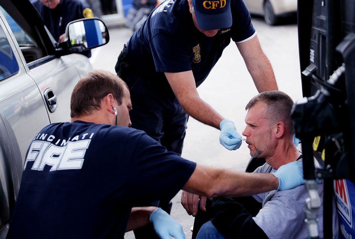 Medics with the Cincinnati Fire Department work to keep a possible overdose victim awake after administering Naloxone while responding to a report at a gas station (AP Photo/John Minchillo)
