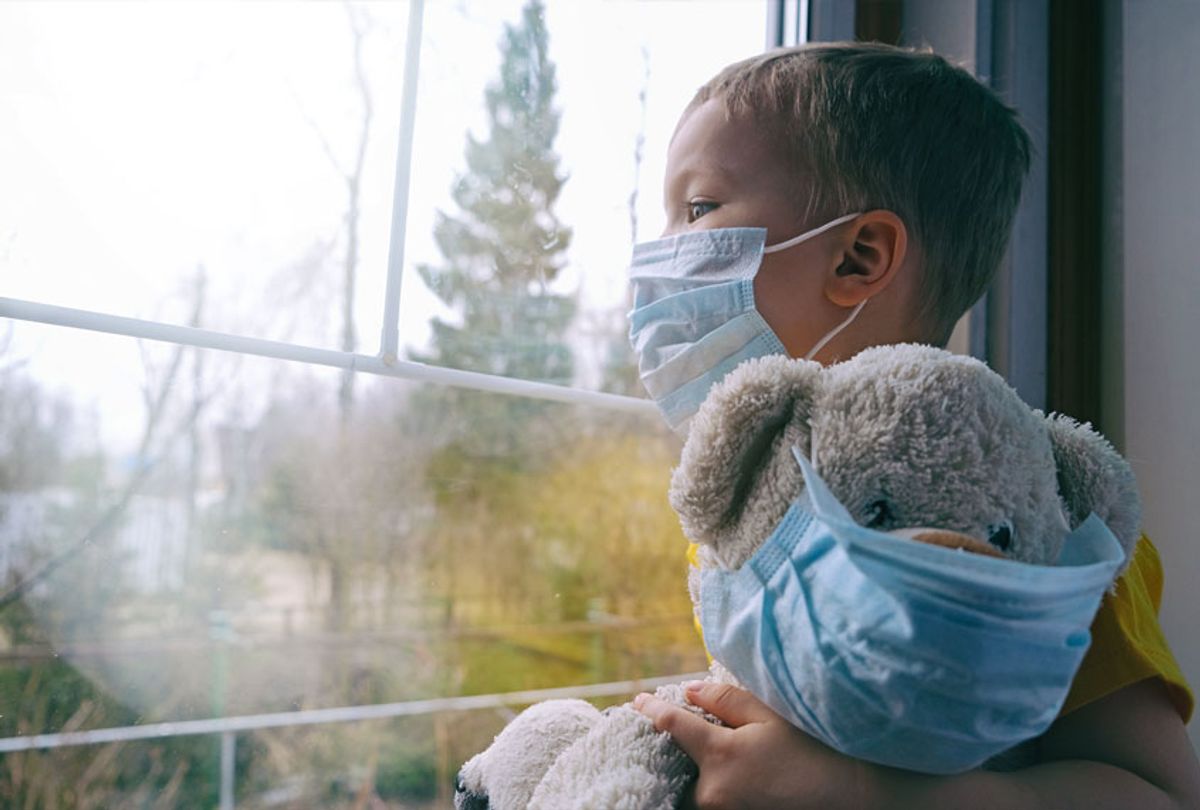 Boy and his teddy bear both in protective medical masks sits on windowsill and looks out window (Getty Images)