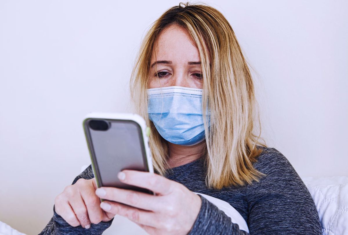 Woman coughing and suffering in medical mask inside the home bedroom, searching for her symptoms on her phone (Getty Images)
