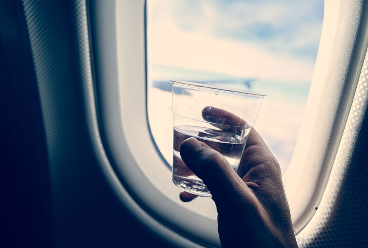 Man's hand holding a glass with transparent liquid (water or liquor), inside an airplane (Getty Images)