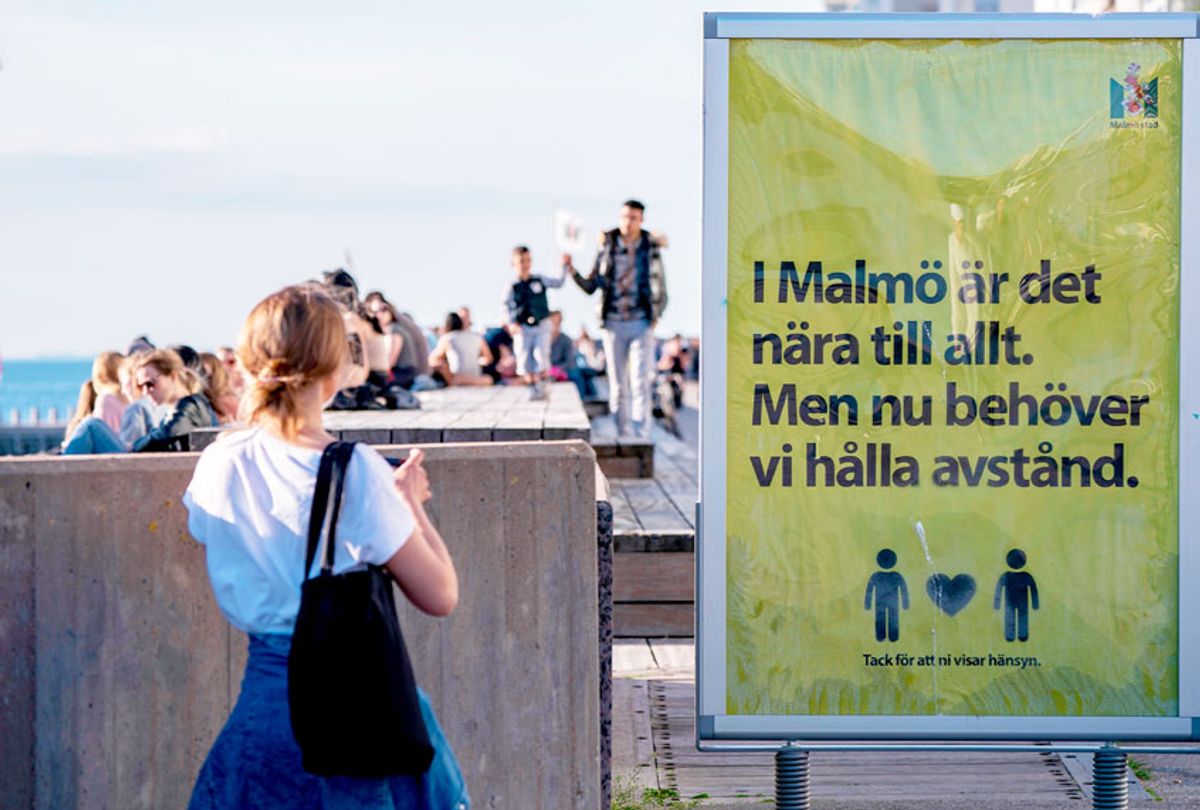 People enjoy the warm evening at Sundspromenaden in Malmo, Sweden, on May 26, 2020, amid the coronavirus pandemic. - The sign reads 'In Malmo everything is near. But now, we need to keep distance'. (JOHAN NILSSON/TT News Agency/AFP via Getty Images)