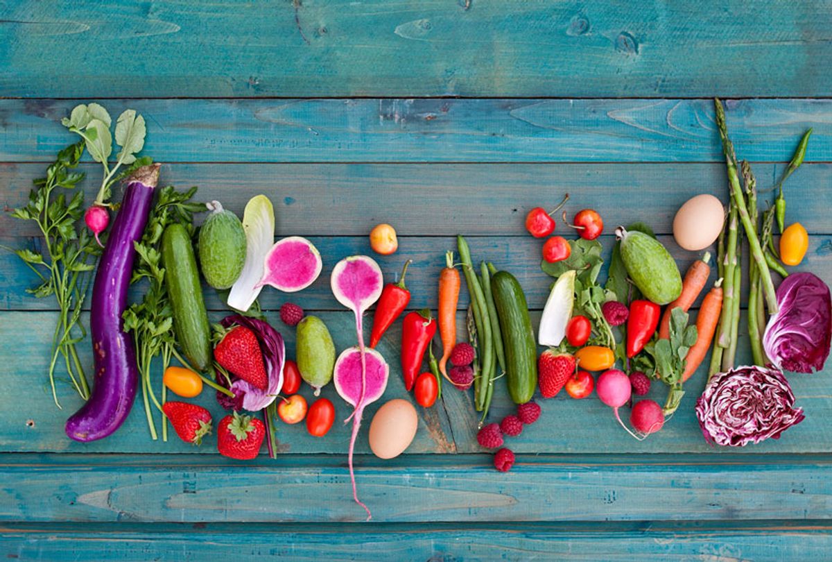 Herbs, eggplant, cucumbers, strawberries, tomatoes, radicchio, watermelon radishes, peppers, eggs, carrots, and asparagus on blue wood surface (Getty Images)