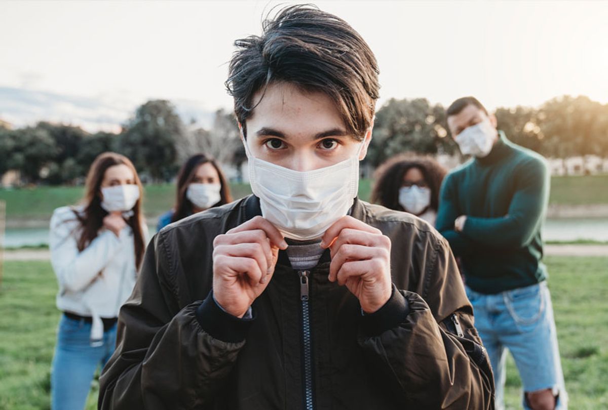 Young adult man wearing a pollution mask to protect himself from viruses. His friends are in the background. They all are wearing masks. (Getty Images)