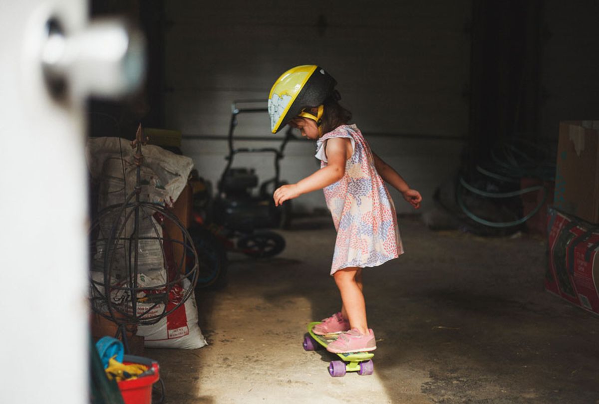Side view of girl wearing helmet while standing on skateboard in garage (Getty Images)