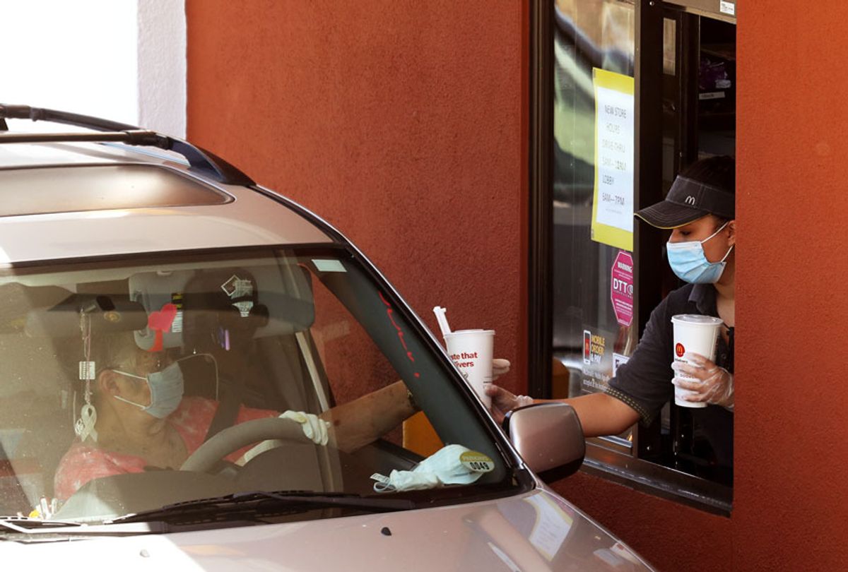  A worker wears a mask and gloves as she hands soft drinks to a customer at a McDonald's drive-thru on April 22, 2020 in Novato, California. (Justin Sullivan/Getty Images)