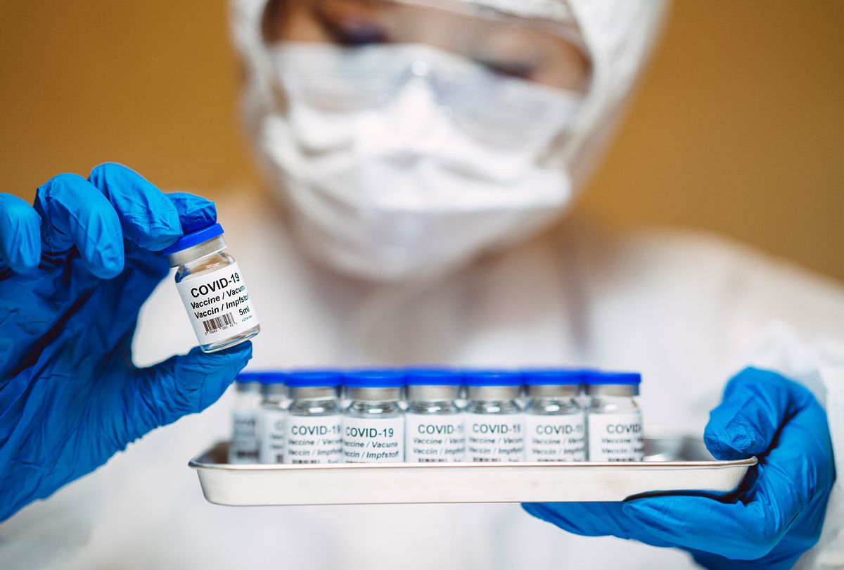 Healthcare professional in protective gloves & workwear holding & organizing a tray of COVID-19 vaccine vials (Getty Images)