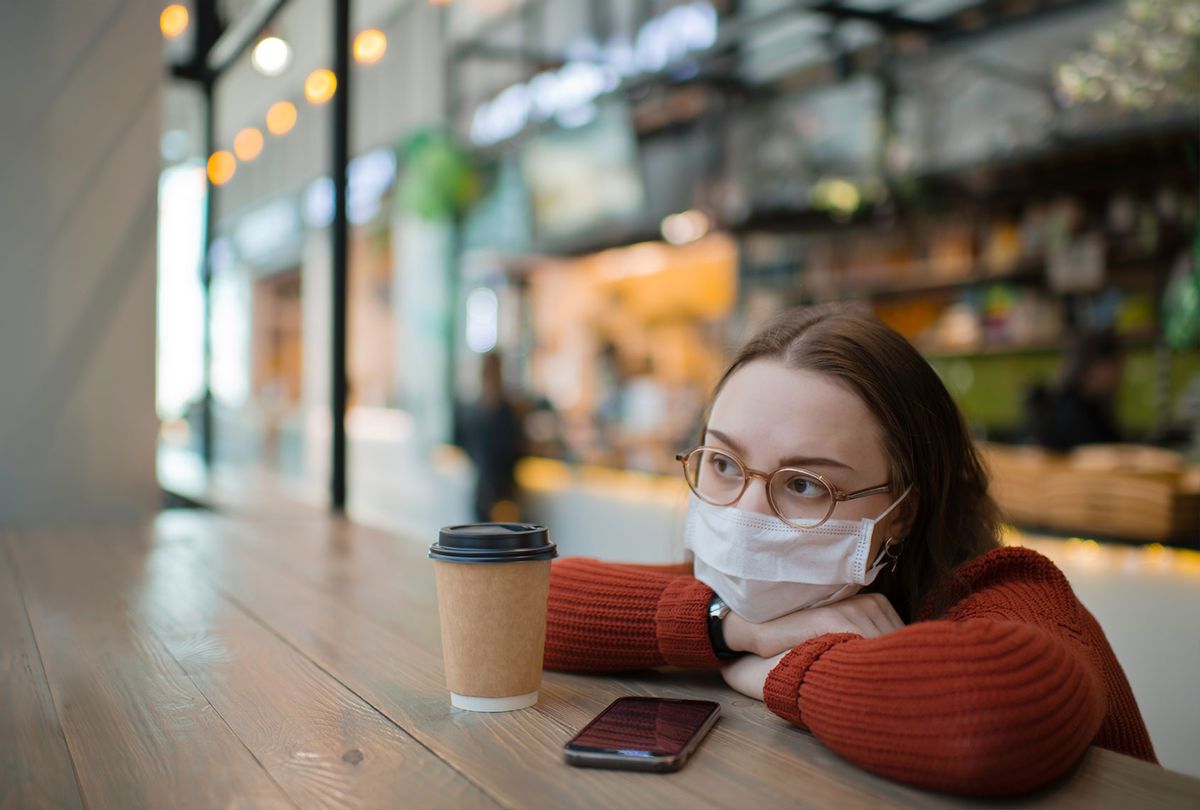Teenager wearing medical mask protecting herself against virus in a food court of a shopping mall or airport lobby with reusable coffee cup (Getty Images)