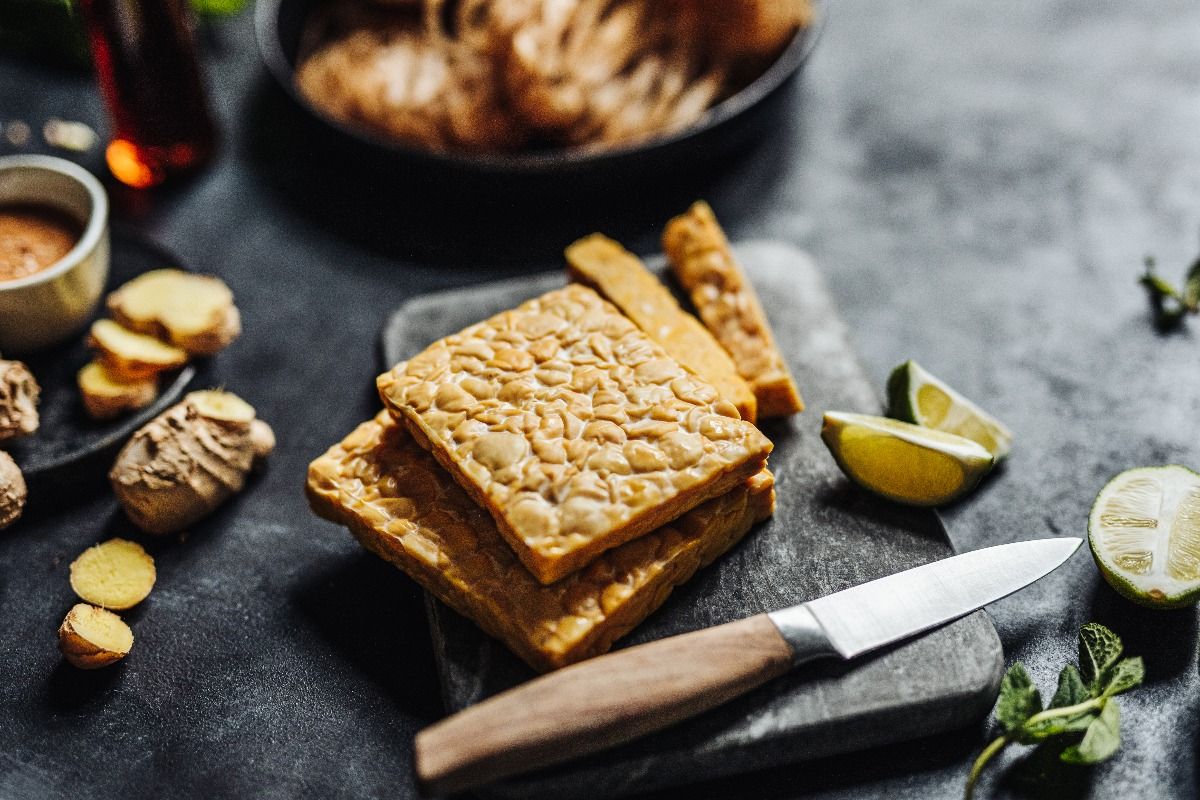 Close-up of tempeh on a cutting board with a kitchen knife with other ingredients. (Getty Images)