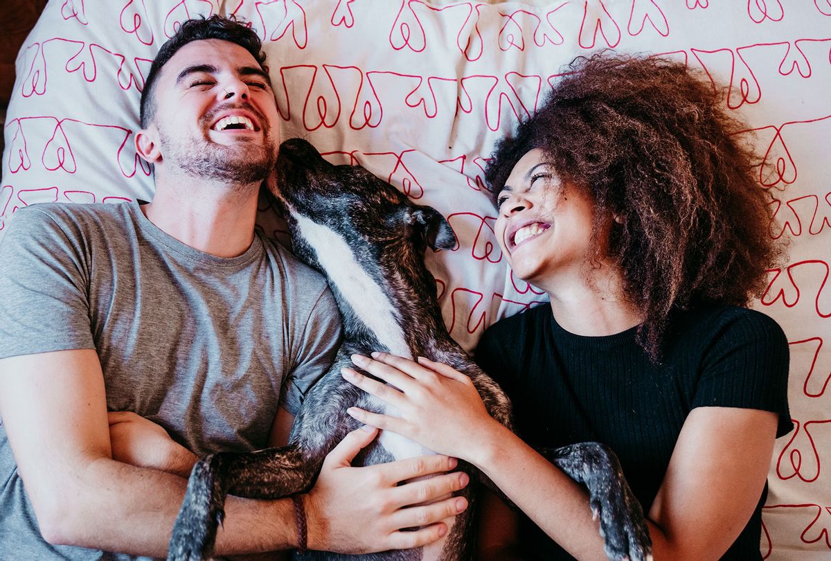 Laughing Couple Lying On Bed With Dog At Home (Getty images)