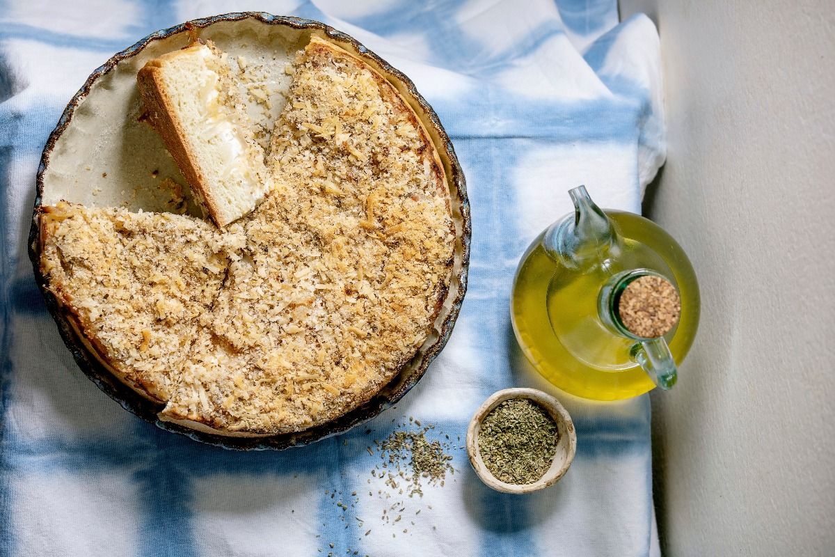 Traditional baked bread sliced cake with onion, herbs and cheese in ceramic dish served with olive oil on blue and white tablecloth. (Photo by: Natasha Breen/REDA&CO/Universal Images Group via Getty Images)