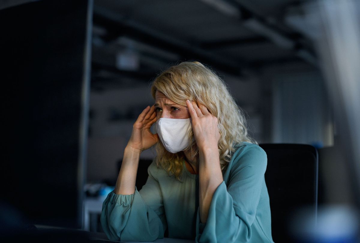 Tired businesswoman with face mask sitting indoors in office, feeling headache (Getty Images)