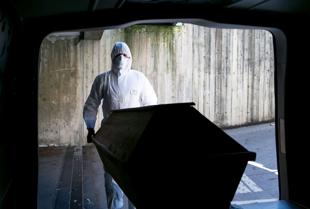 Undertaker worker dressed in full protective clothing and mask pushes a coffin carrying a deceased Covid-19 victim into a mortuary van at a morgue on April 2, 2020. (Jan Hetfleisch/Getty Images)