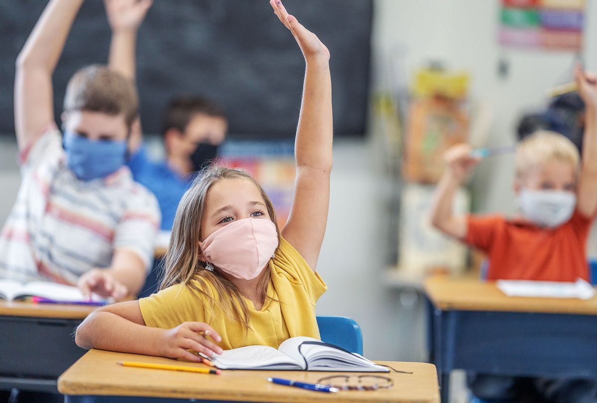 Group of students wearing protective face masks while raising their hands in class. (Getty Images/Fat Camera)
