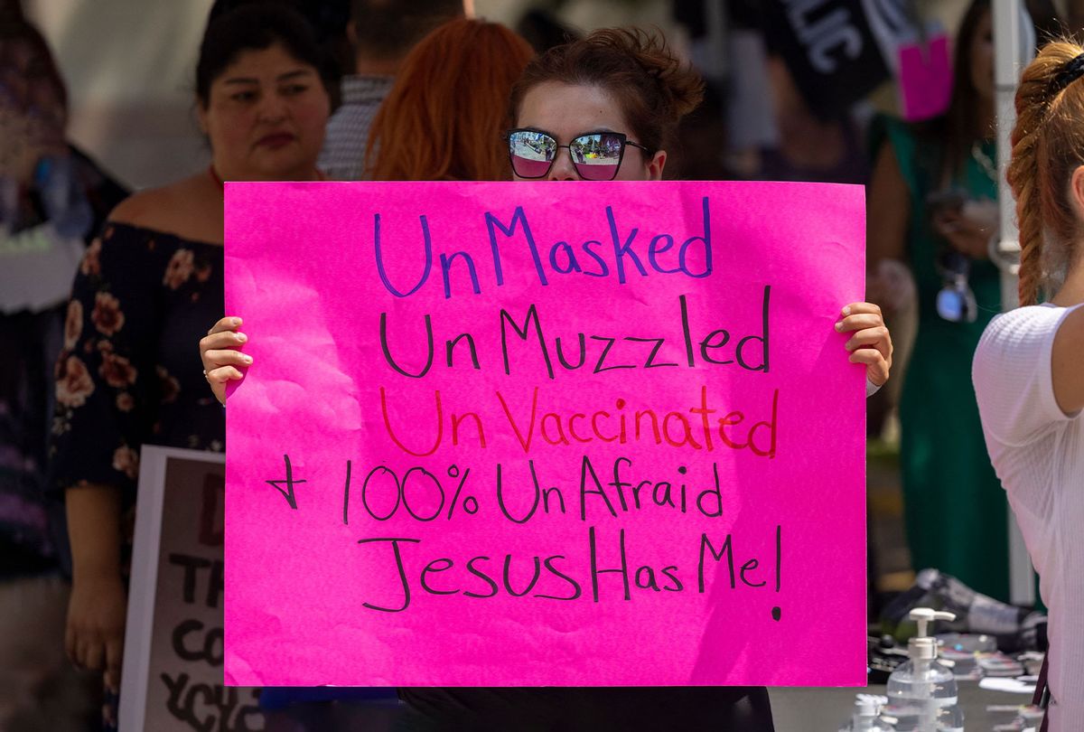 A woman holds a sign proclaiming her belief that she doesn't need to be vaccinated or wear a mask because Jesus will protect her from coronavirus, as anti-vaccination protesters pray and rally near City Hall after the Los Angeles City Council voted earlier this week to create an ordinance requiring proof of vaccination to enter many indoor public spaces, in Los Angeles, August 14, 2021. (DAVID MCNEW/AFP via Getty Images)