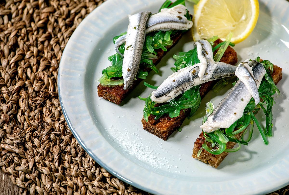 Appetizers tapas pickled anchovies or sardines fillet Wakame seaweed salad on toasted rye bread, served on blue plate with lemon on straw napkin as background. (Natasha Breen/REDA&CO/Universal Images Group via Getty Images)