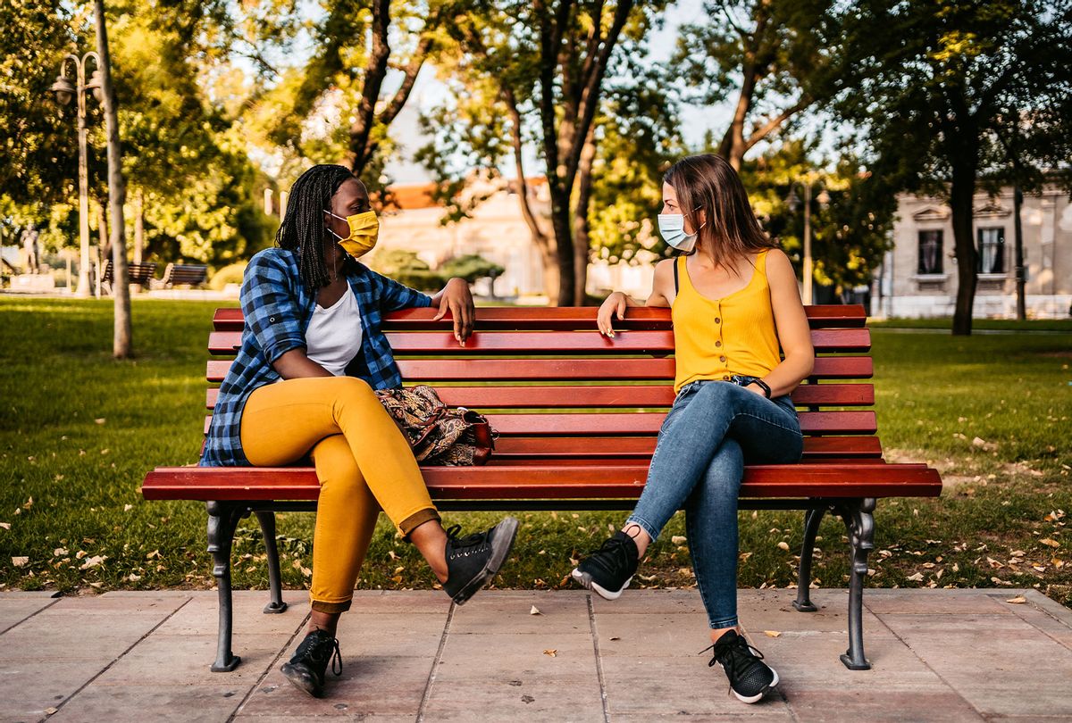 Two women with protective face masks on sitting on park bench with social distance between. (Getty Images)