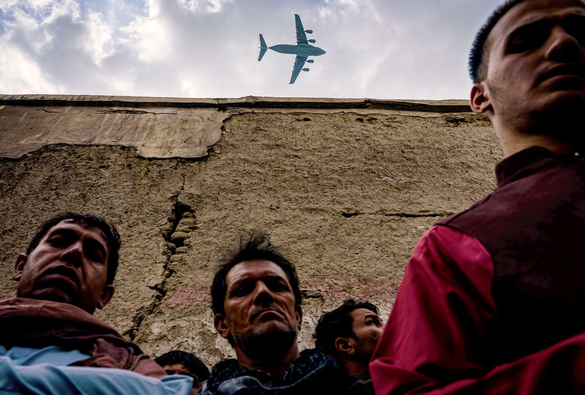 A military transport plane flies over as Relatives and neighbors of the Ahmadi family gathered around the incinerated husk of a vehicle targeted and hit earlier Sunday afternoon by an American drone strike, in Kabul, Afghanistan, Monday, Aug. 30, 2021. (Getty Images/MARCUS YAM/LOS ANGELES TIMES)