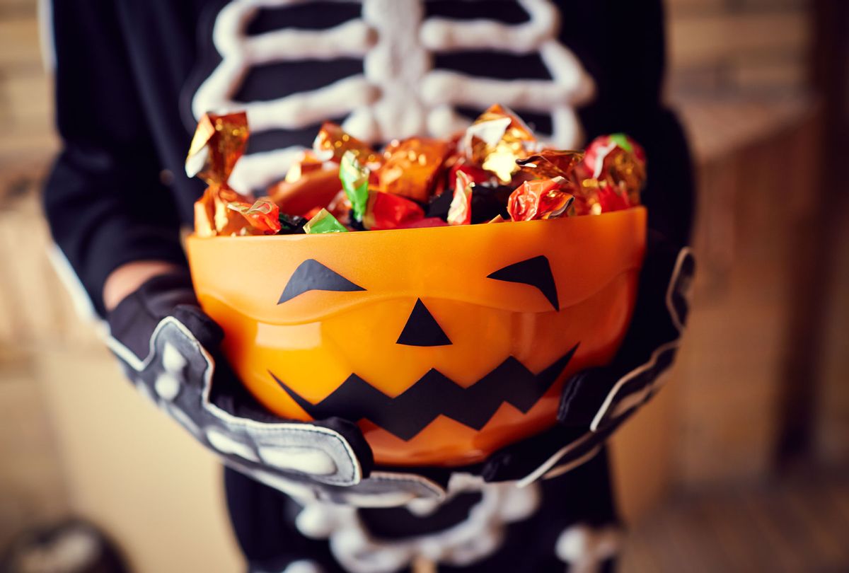 Boy in skeleton costume holding bowl full of candies (Getty Images/mediaphotos)