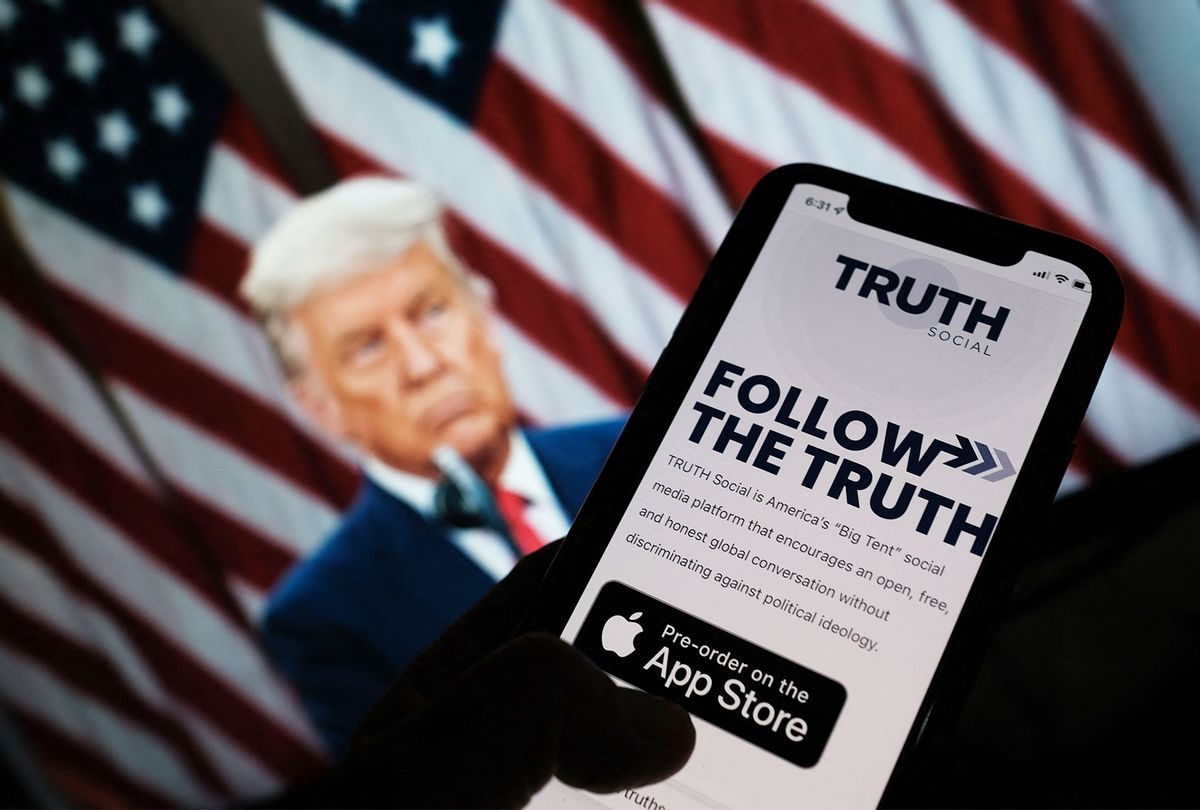 This illustration photo shows a person checking the app store on a smartphone for "Truth Social", with a photo of former US president Donald Trump on a computer screen in the background, in Los Angeles, October 20, 2021. (CHRIS DELMAS/AFP via Getty Images)