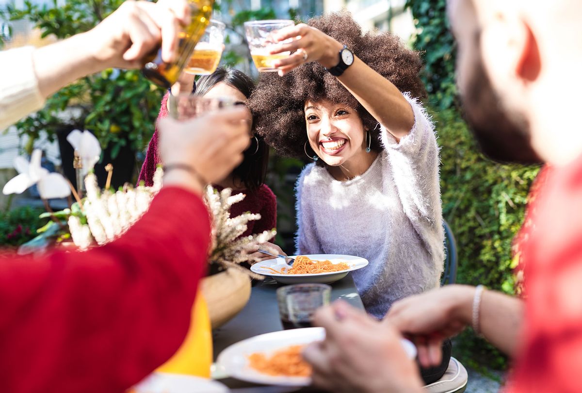 Friends eating meal together outdoors, raising a toast with drinks (Getty Images/Eugenio Marongiu)