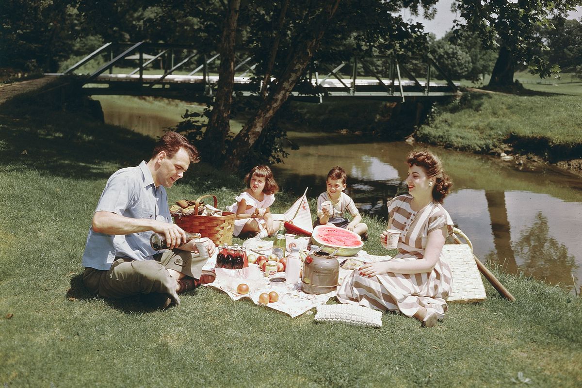 A man pours drinks from a bottle as his family has a picnic meal in the grass beside a pond, circa 1948. (Lambert/Getty Images)