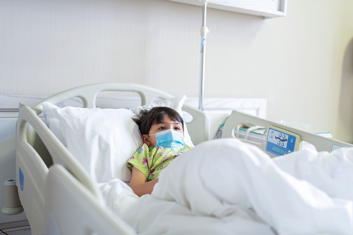 Little child patient with protective face mask lying on bed at hospital (Getty Images/aquaArts studio)