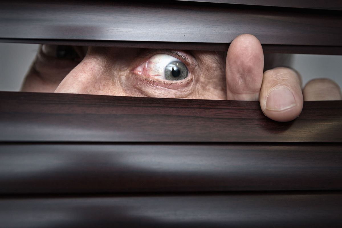 Wild-eyed man peeking ominously through the blinds (Getty Images/RapidEye)