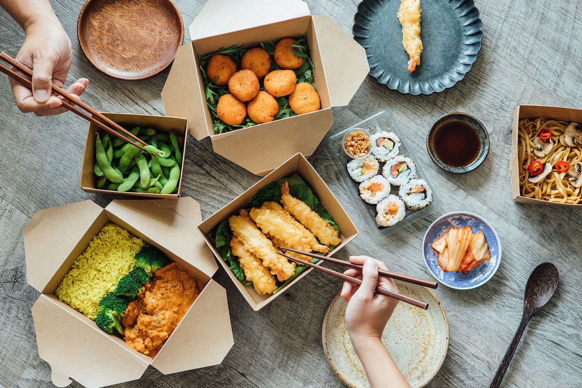 Flat lay of two people’s hands using chopsticks while sharing assorted takeaway Asian food at the dining table (Getty Images/Oscar Wong)