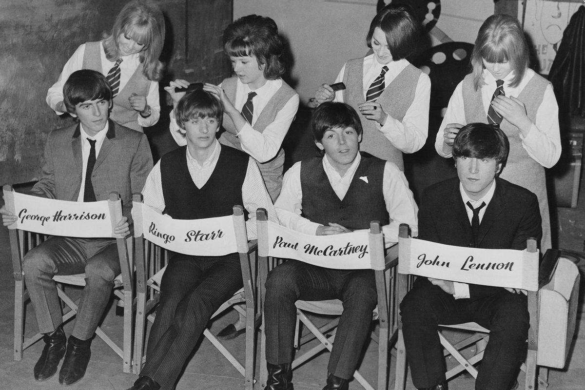 British rock band The Beatles sitting backward in director's chairs with their name across the backrest, with British fashion model Pattie Boyd (behind Harrison), Tina Williams (behind Starr), Prudence Bury (behind McCartney), and Susan Whitman (behind Lennon), pretending to adjust the Beatles' hair on the set of 'A Hard Day's Night', location unspecified, United Kingdom, 1964. (Archive Photos/Getty Images)