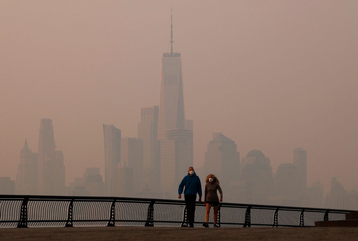 People wearing masks walk along the Hudson River as smoke shrouds the skyline of lower Manhattan and One World Trade Center as the sun rises in New York City on June 8, 2023. (Gary Hershorn/Getty Images)