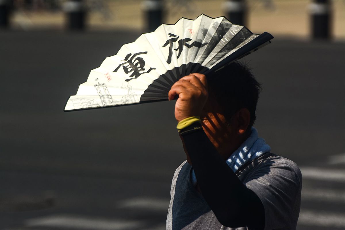 A man is seen blocking the sun with a fan at Shanghai, China, on July 6, 2023 as Shanghai issues an orange alert for the continuous heatwave. (Ying Tang/NurPhoto via Getty Images)