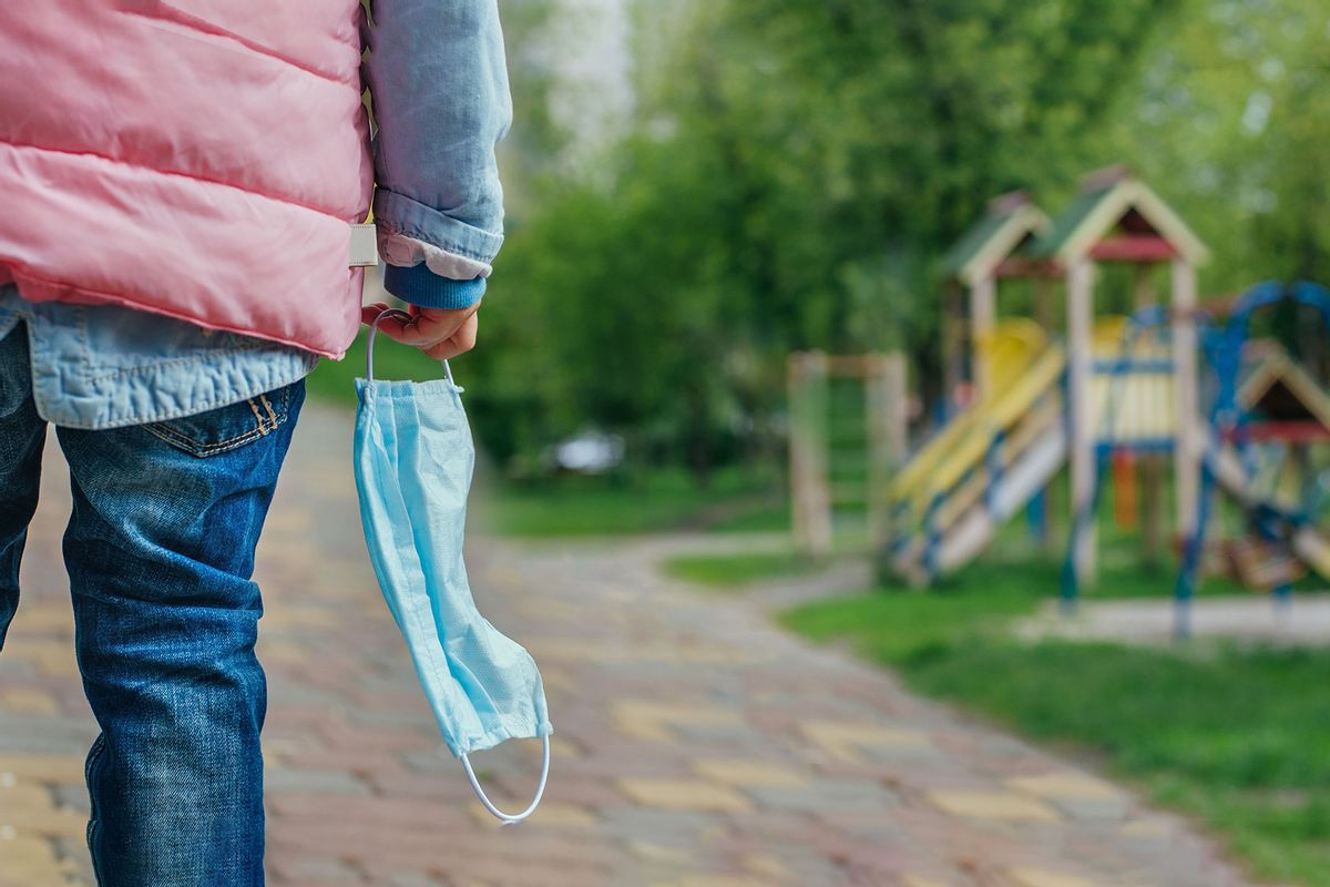 A little girl holding her protective face mask looking at the open playground (Getty Images/lithiumcloud)